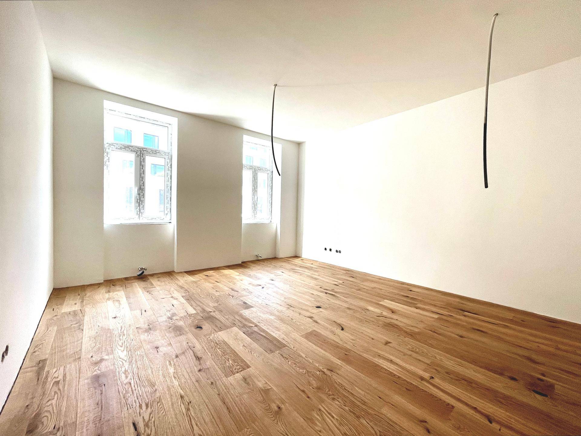 Geräumiger, heller Raum mit neuem Holzparkettboden und zwei großen Fenstern, bereit zum Einzug.