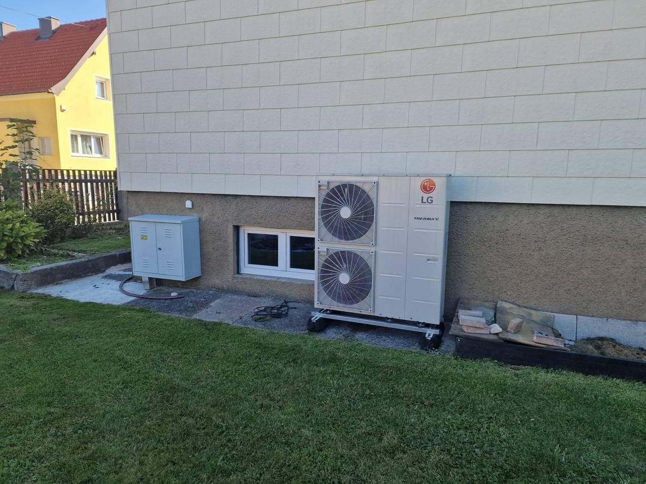 Detailansicht der Wärmepumpe an der Hauswand mit angrenzendem Rasenbereich.