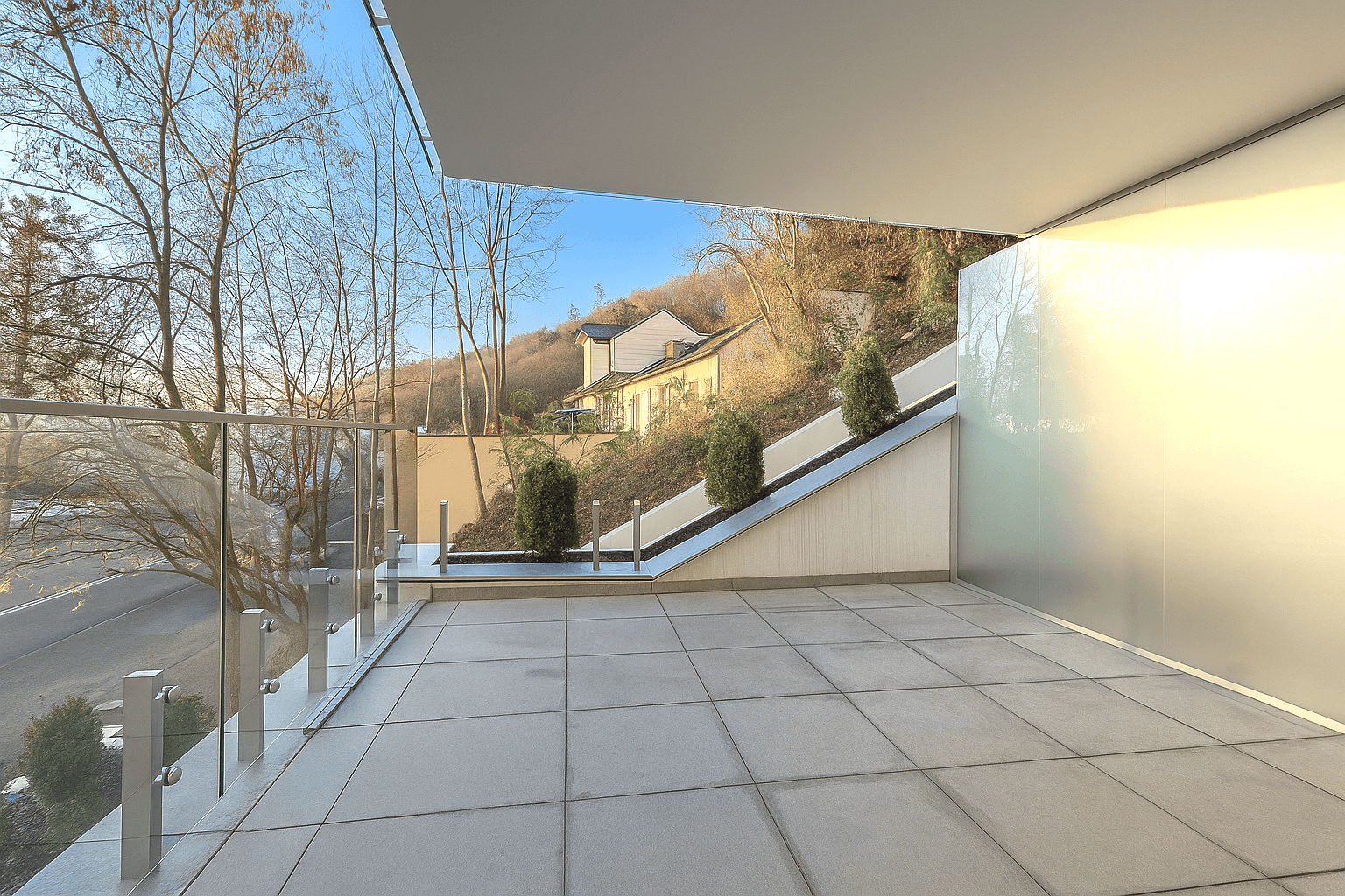 Moderner Balkon mit Glasgeländer und Blick auf die umliegende Landschaft und Häuser.