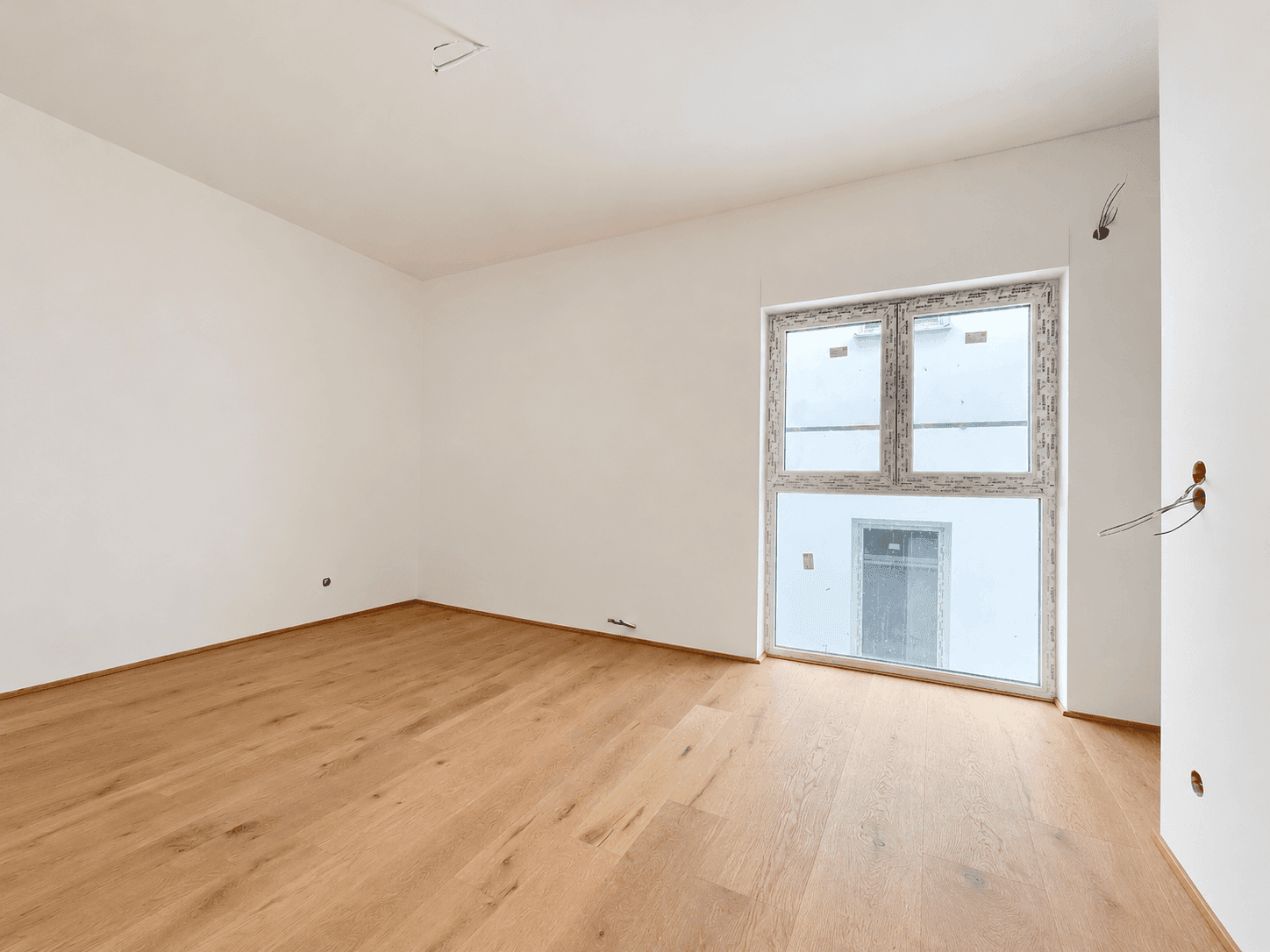 Unmöbliertes Zimmer mit hellem Parkettboden und einem großen Fenster, ideal für ein Schlafzimmer.