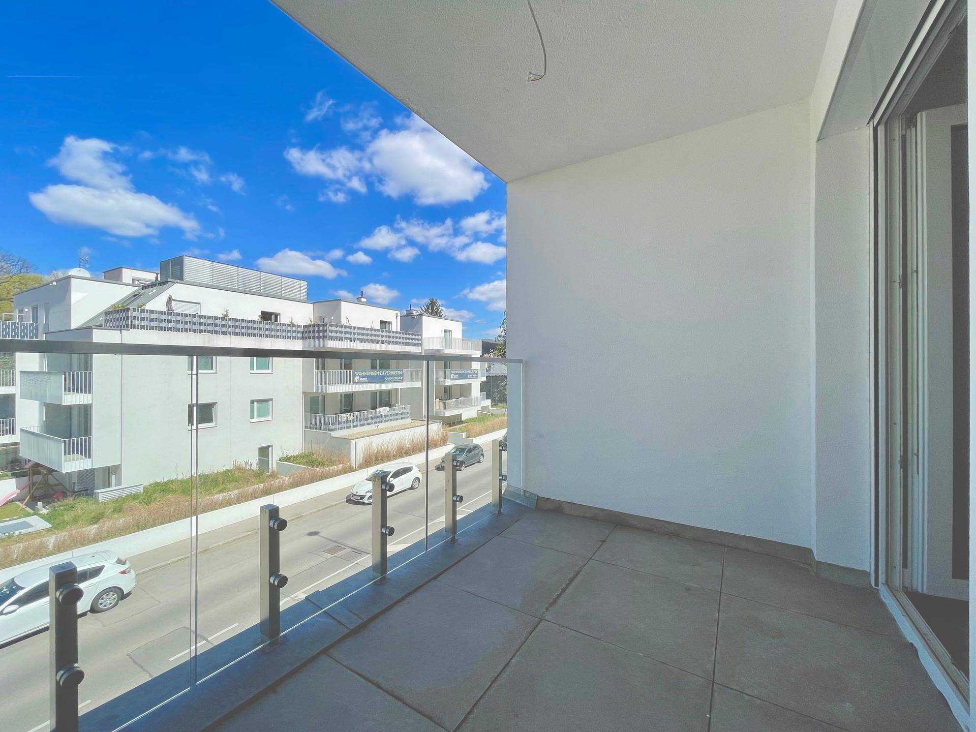 Schmaler Balkon mit Fliesenboden und Glasgeländer, bietet einen Blick auf die Straße und die Umgebung.