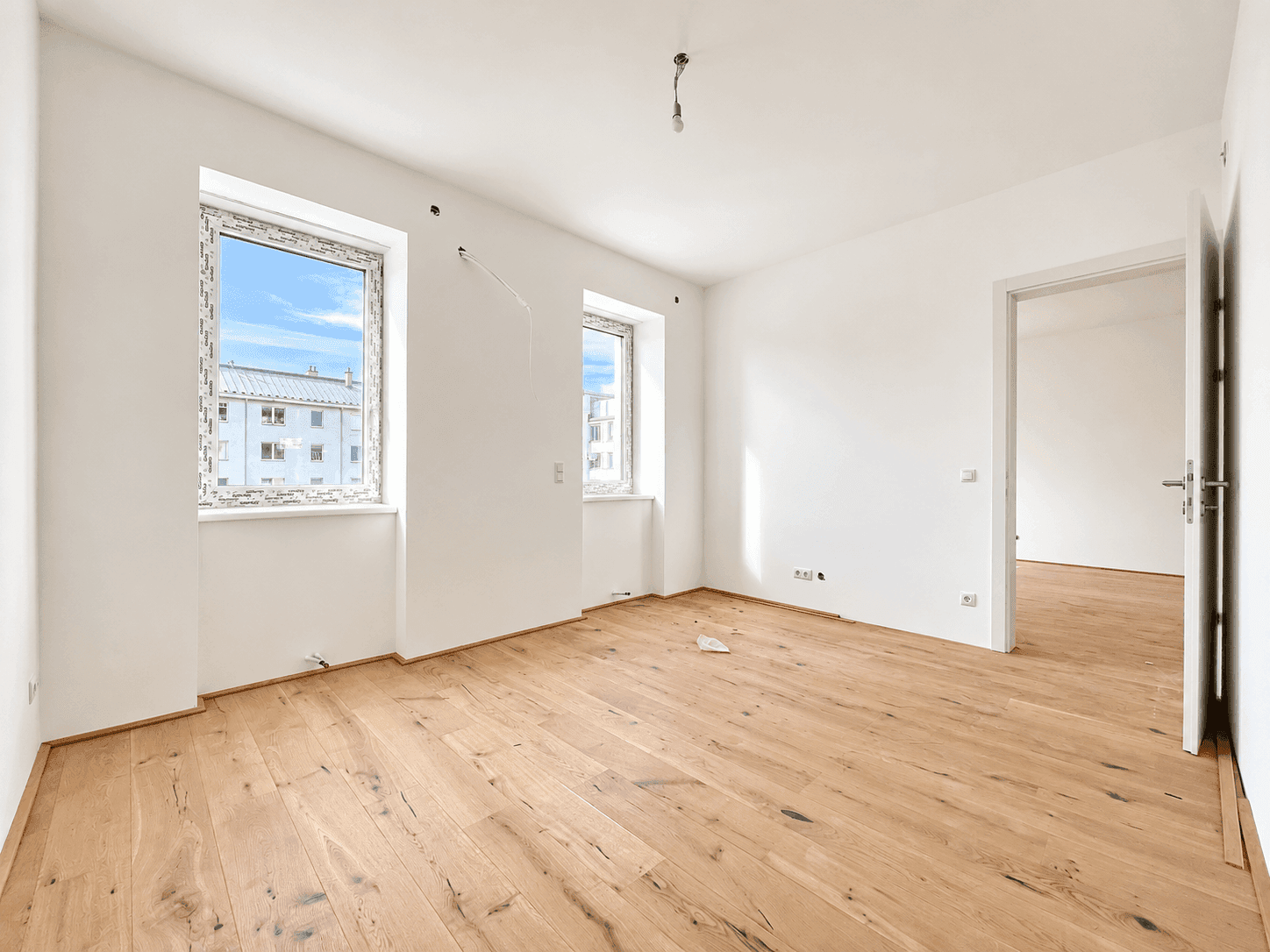 Unmöblierter Raum mit zwei Fenstern und hellem Parkettboden, ideal für ein Wohn- oder Schlafzimmer.