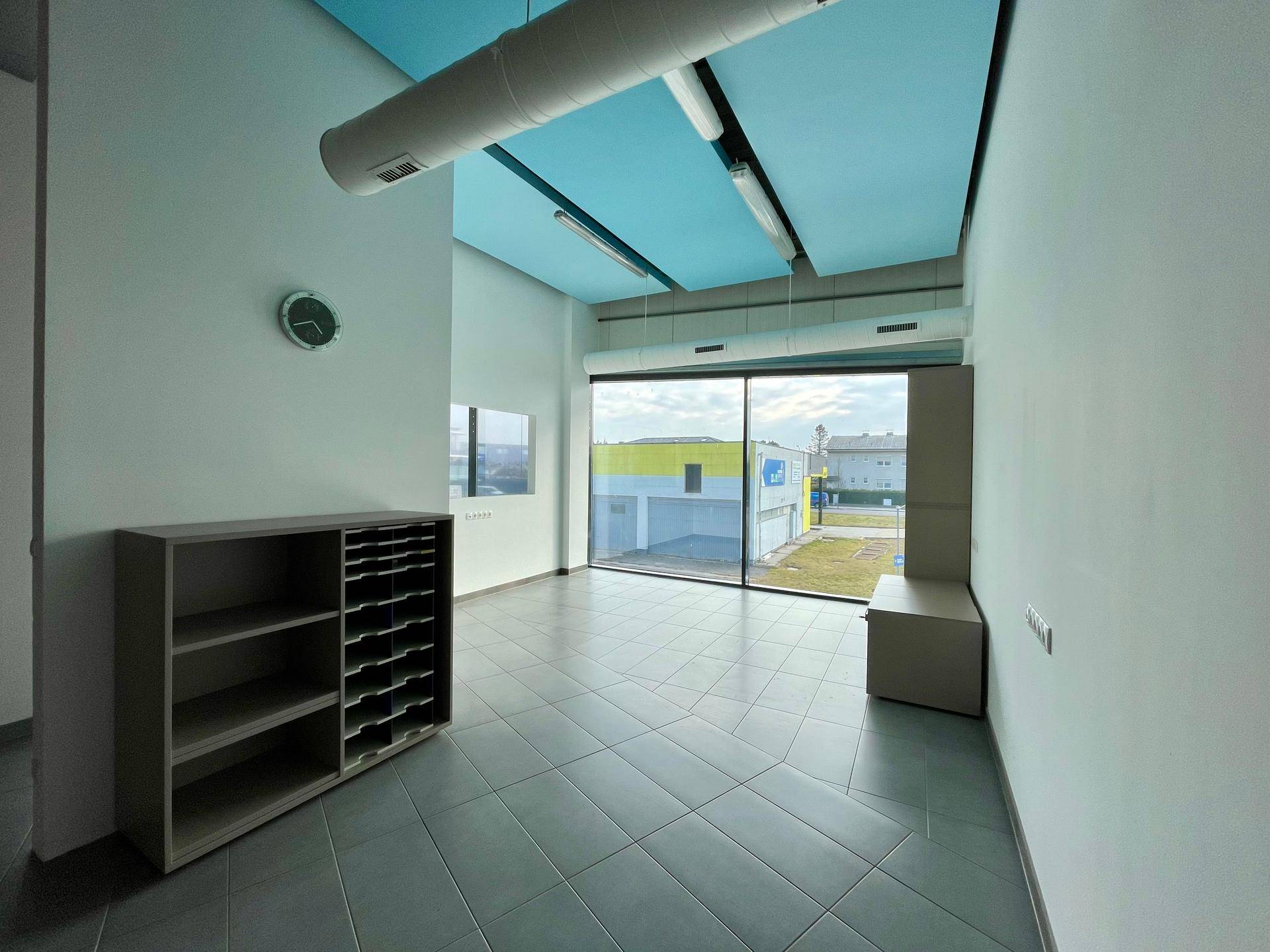 Leeres Büro mit großen Fenstern, hellblauen Deckenpaneelen und grauem Fliesenboden, bereit zur Einrichtung.