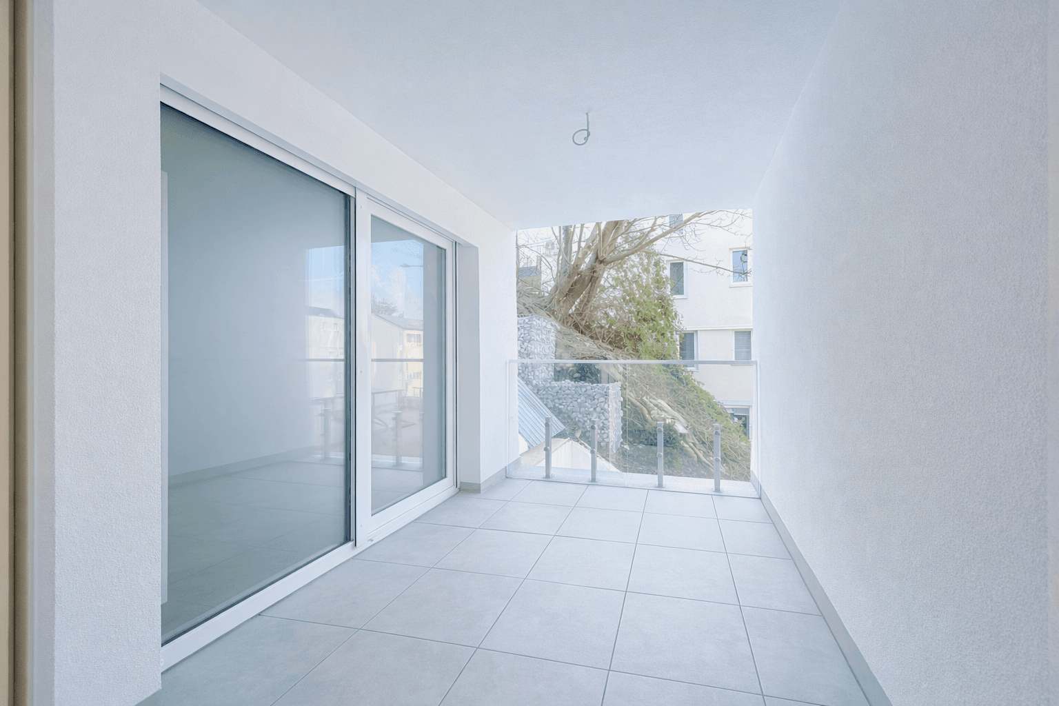 Schmaler Balkon mit Fliesenboden und Glasgeländer, bietet direkten Zugang zum Innenbereich.