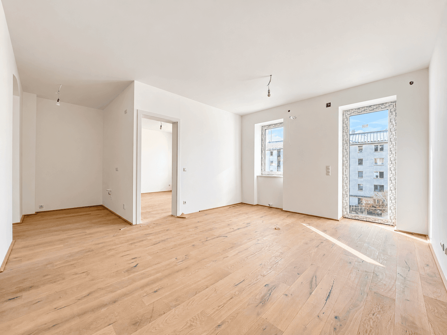 Heller Wohnraum mit Holzboden und großen Fenstern, ideal für offenes Wohnen.