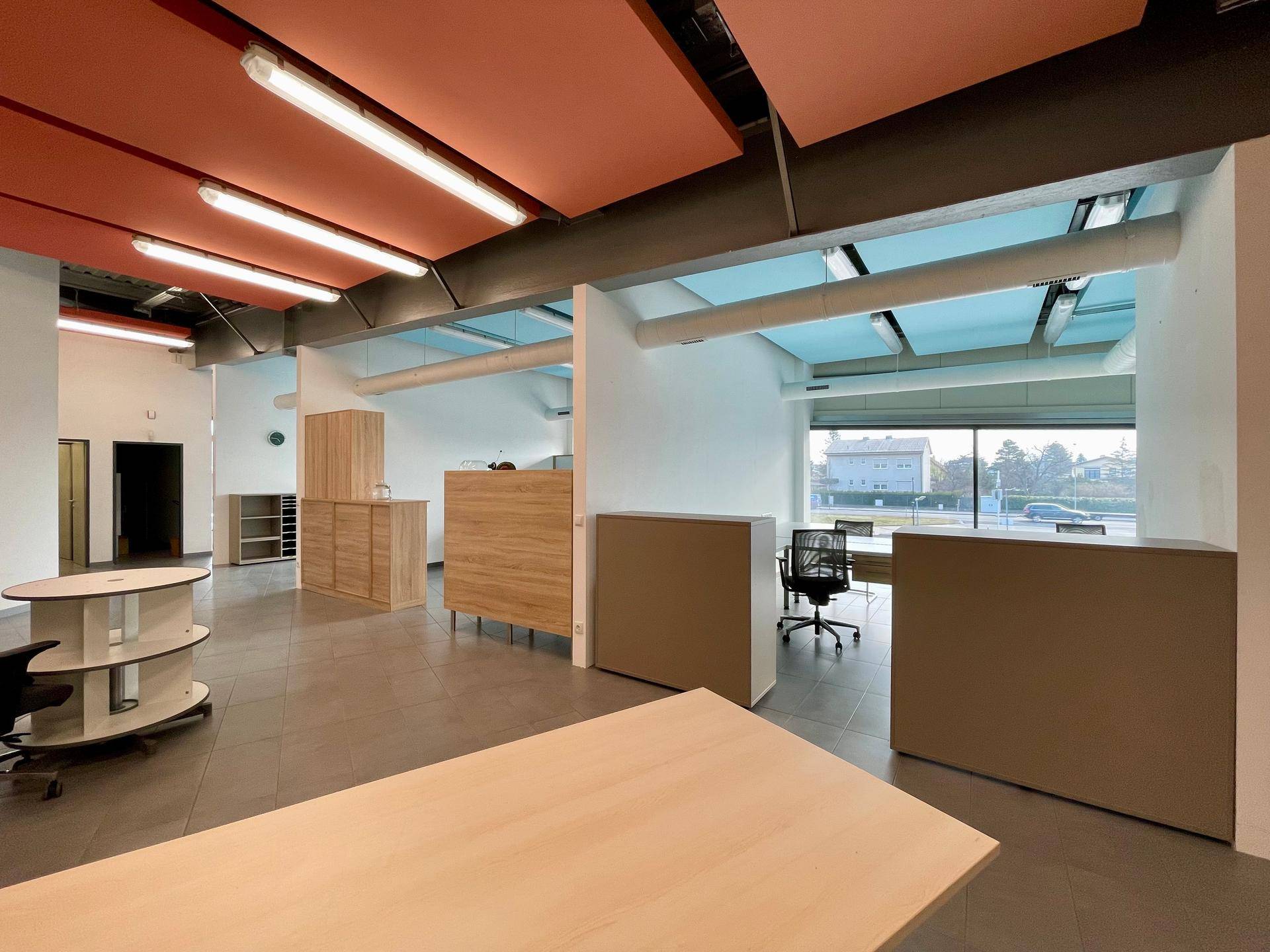 Offener Bürobereich mit farbigen Deckenpaneelen, grauem Fliesenboden und großen Fenstern, schafft eine moderne Arbeitsumgebung.