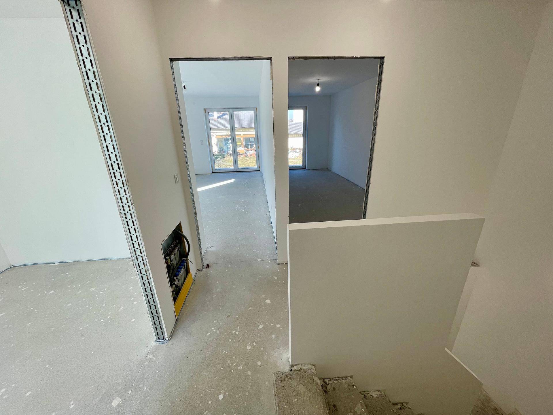 Flurbereich im Rohbau mit Treppenaufgang und Blick in angrenzende Zimmer.