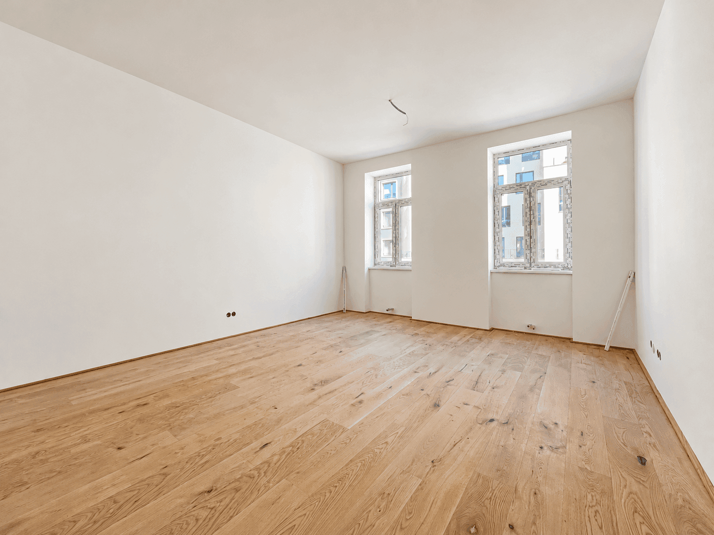 Geräumiger, unmöblierter Raum mit hellem Holzfußboden und viel Tageslicht durch die Fenster.
