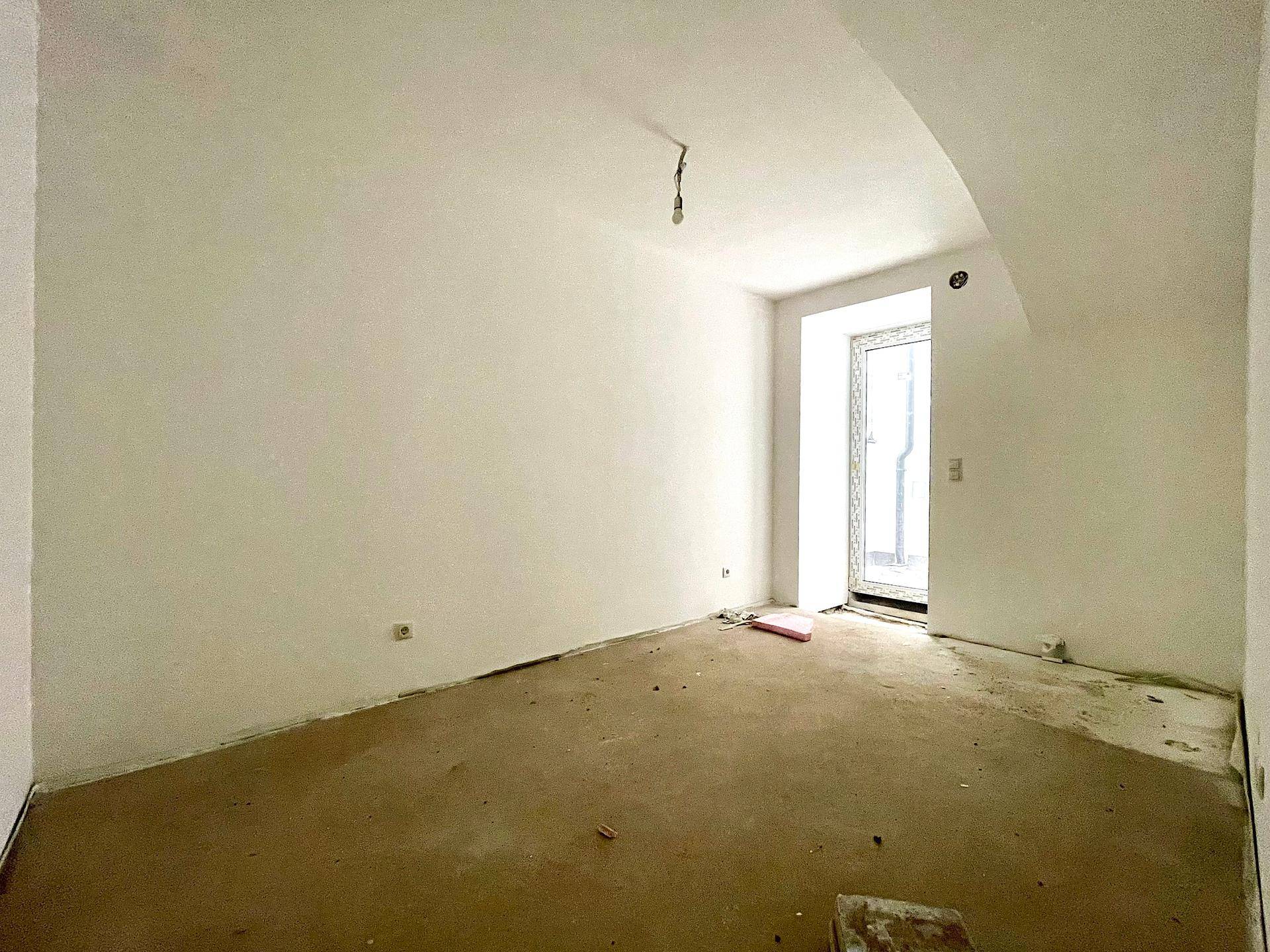 Kleiner, unfertiger Raum mit einer Fenstertür und Rohbauwänden, bereit für den Innenausbau.