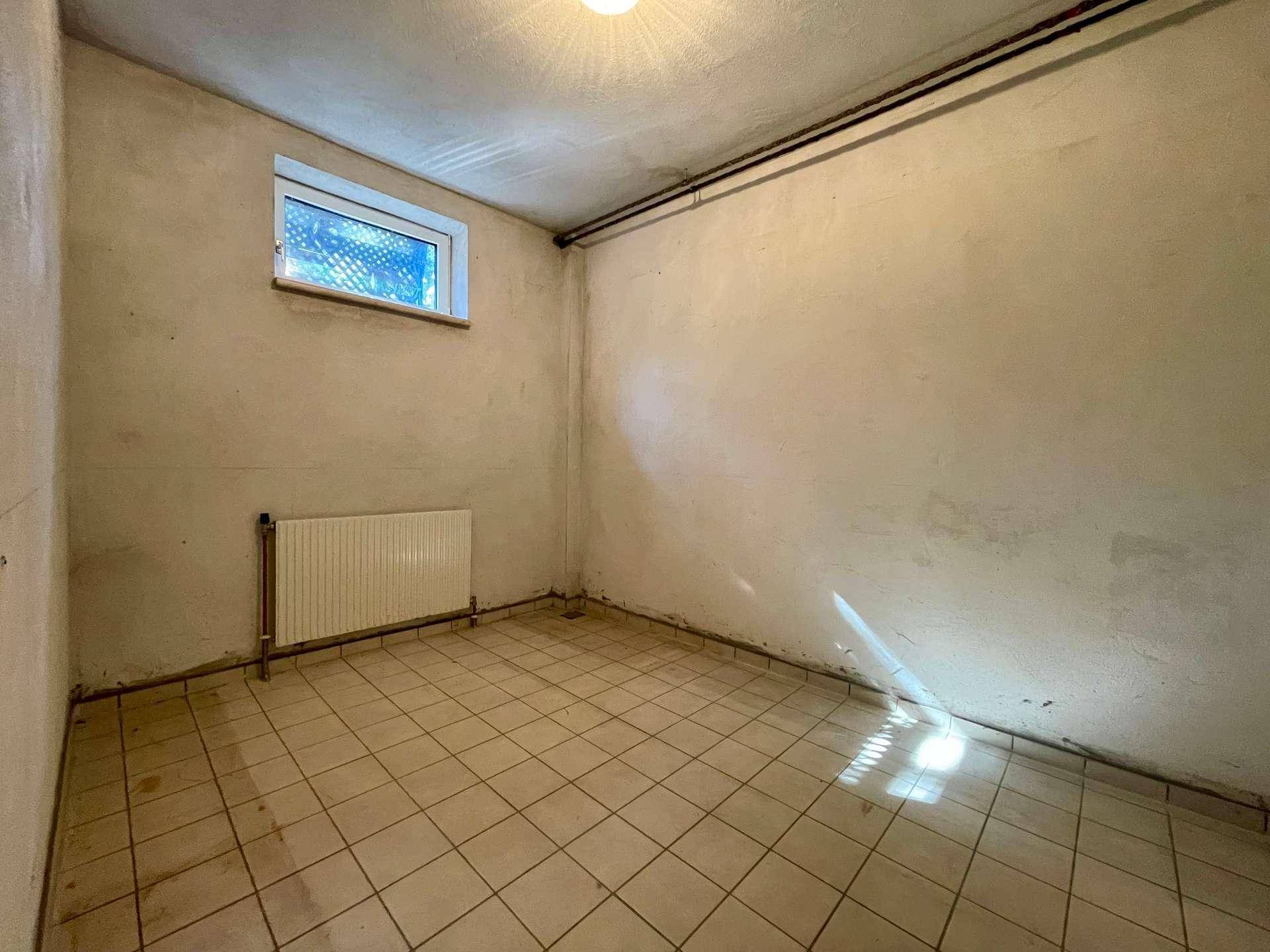 Weiterer Kellerraum mit Fliesenboden und Fenster, geeignet als Lager oder Hobbyraum.