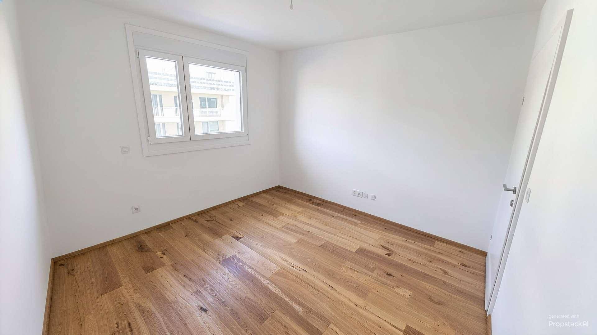 Freundliches Zimmer mit Holzboden und Blick auf die umliegenden Gebäude, ideal als Schlafzimmer.