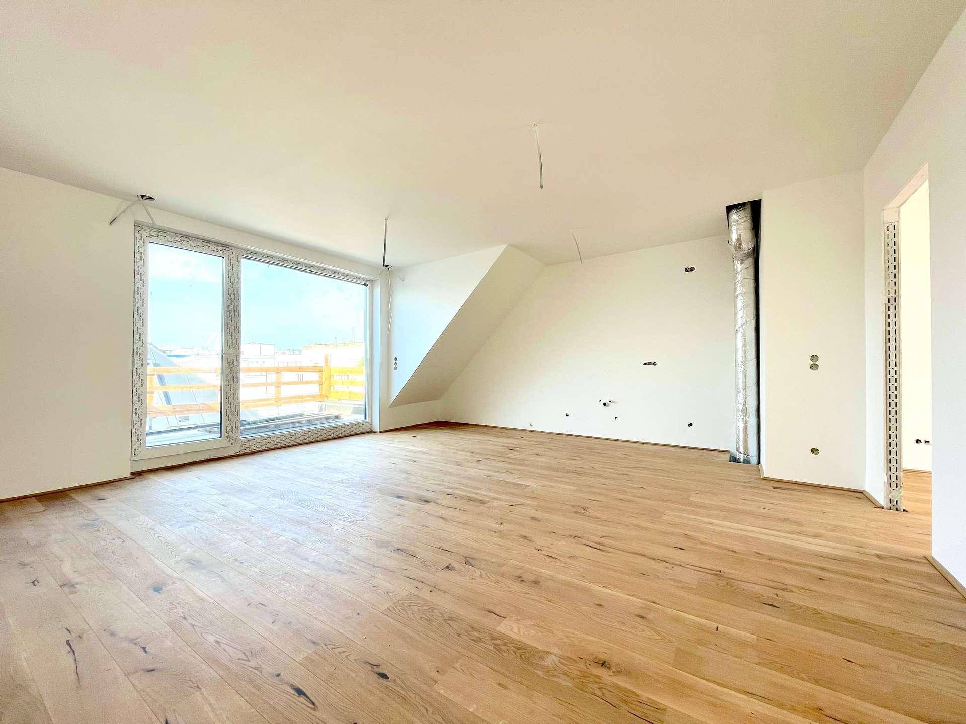 Geräumiger Wohnbereich im Dachgeschoss mit Holzboden und großer Fensterfront, die viel Licht spendet.