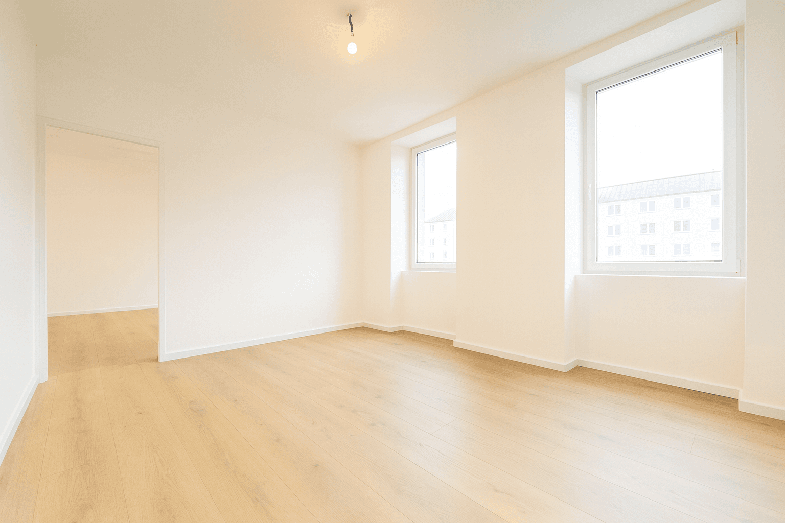 Leerer, heller Raum mit Holzboden und großen Fenstern, bereit zur Einrichtung.