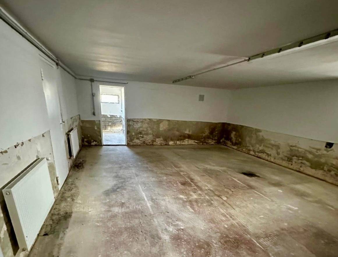 Kellerraum mit sichtbaren Feuchtigkeitsschäden und Heizkörpern, benötigt umfassende Sanierung und Renovierung.