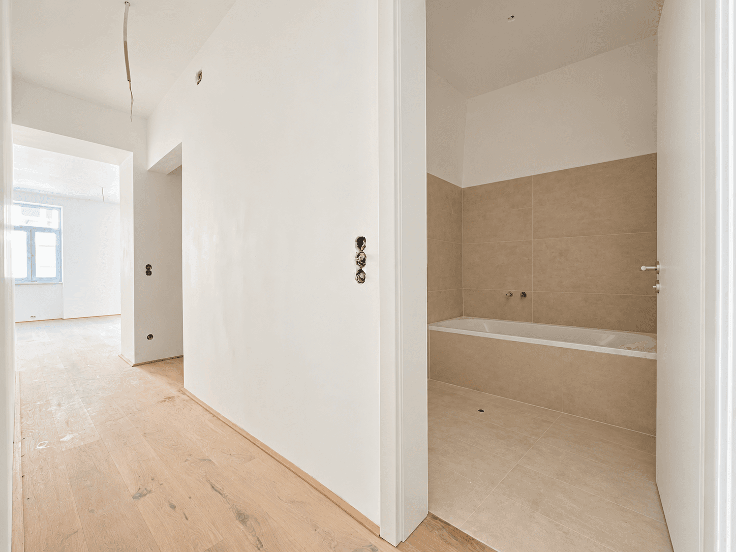 Heller Flur mit Zugang zu einem Badezimmer mit Badewanne und beigefarbenen Fliesen.