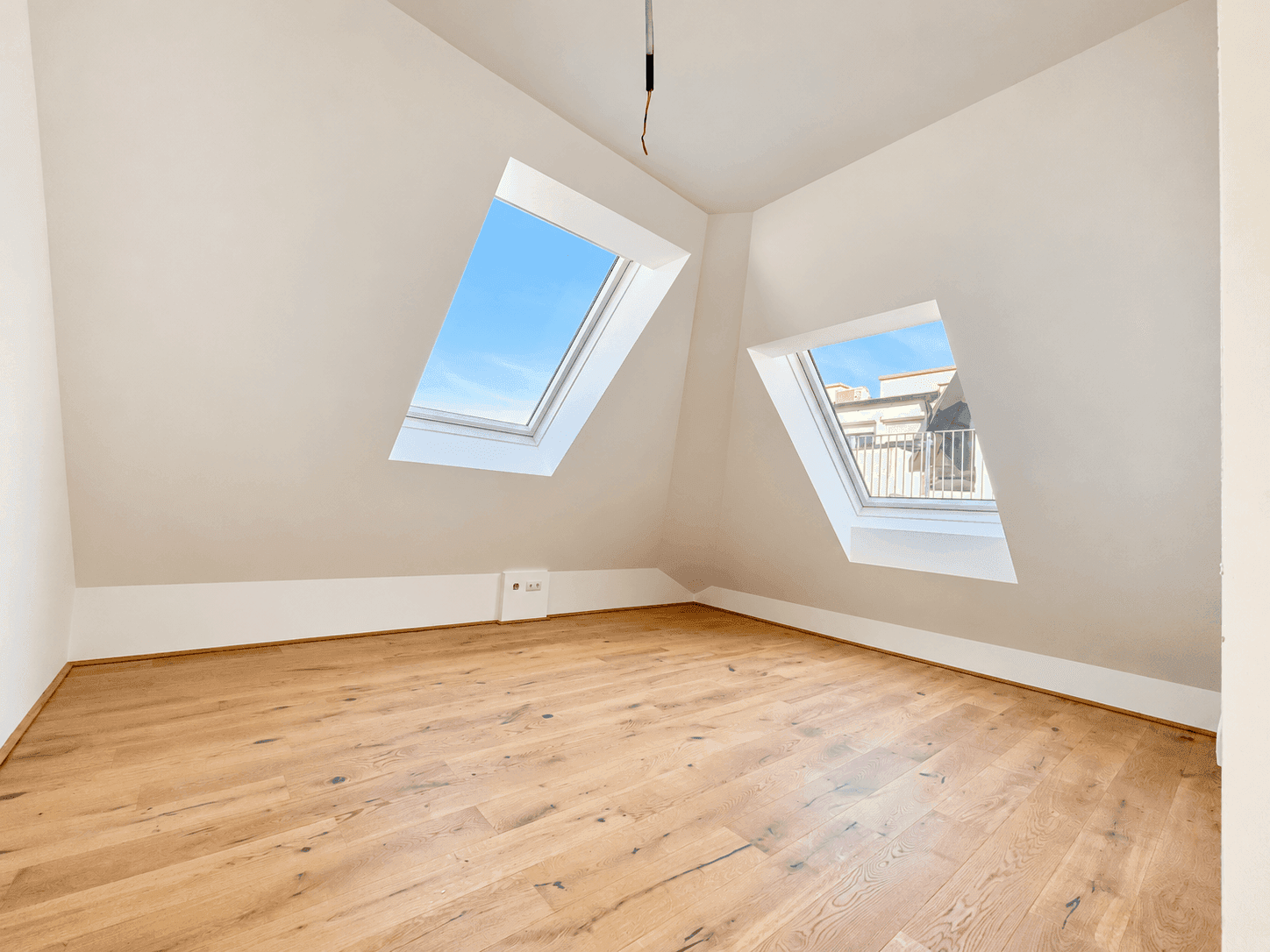 Helles Zimmer mit Holzboden und zwei Dachfenstern, ideal als Schlaf- oder Arbeitszimmer.