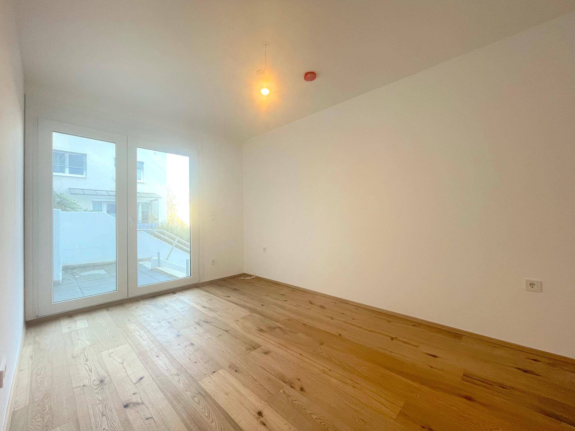 Helles Schlafzimmer mit Holzboden und Zugang zu einer Terrasse, bietet viel Tageslicht.