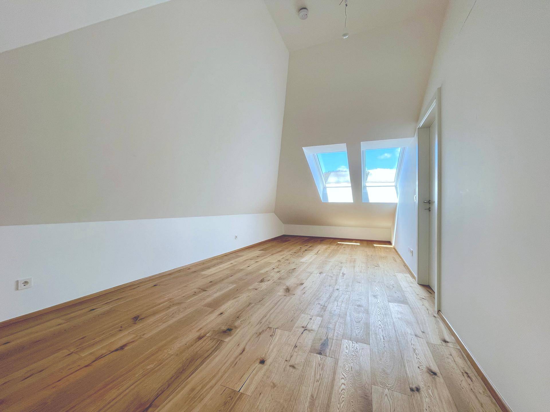 Geräumiges Wohnzimmer im Dachgeschoss mit Holzboden und Dachfenstern, bietet viel Tageslicht.