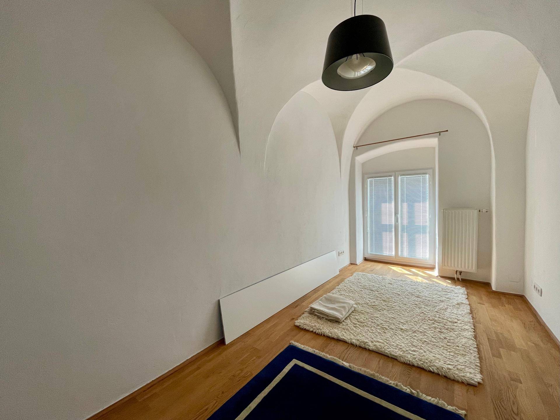 Schlafzimmer mit gewölbter Decke, Holzboden und einem Fenster, das viel Licht hereinlässt.