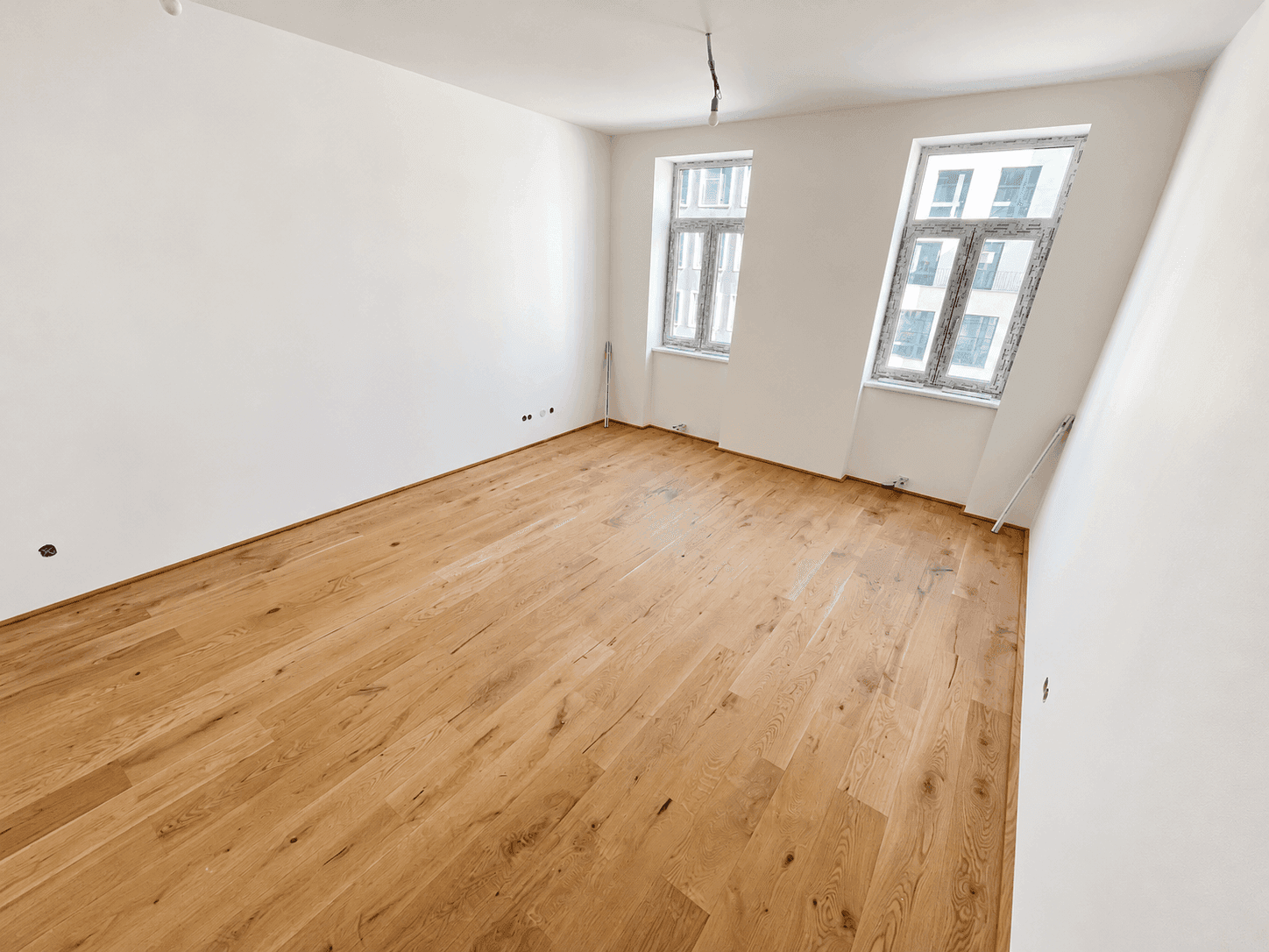 Großer, heller Raum mit attraktivem Holzfußboden und zwei Fenstern, bereit für individuelle Gestaltung.