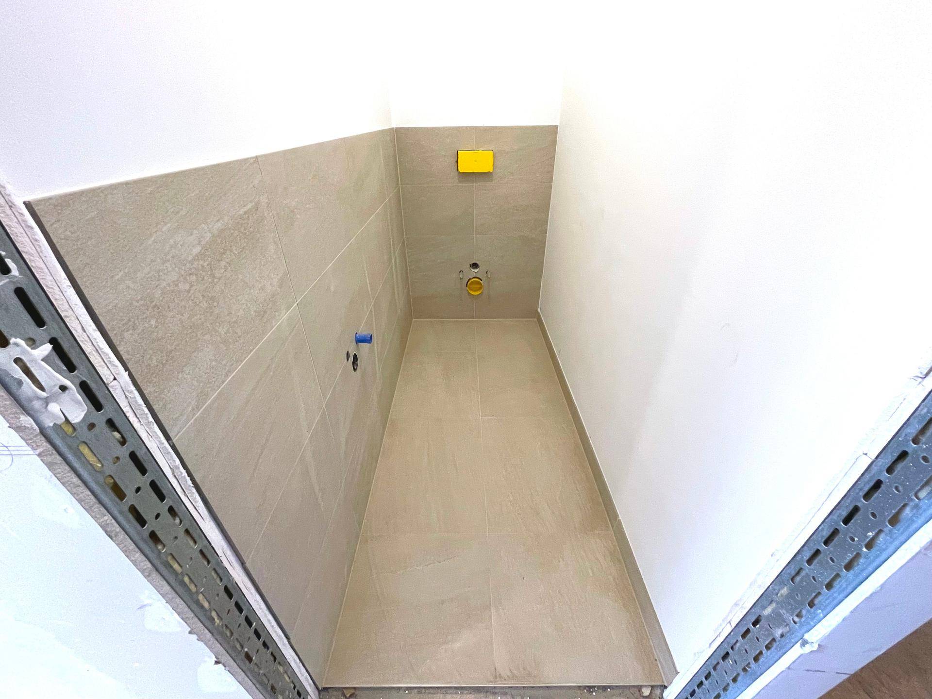 Kleiner Raum mit Fliesen an Wänden und Boden, vorbereitet für die Installation einer Toilette.