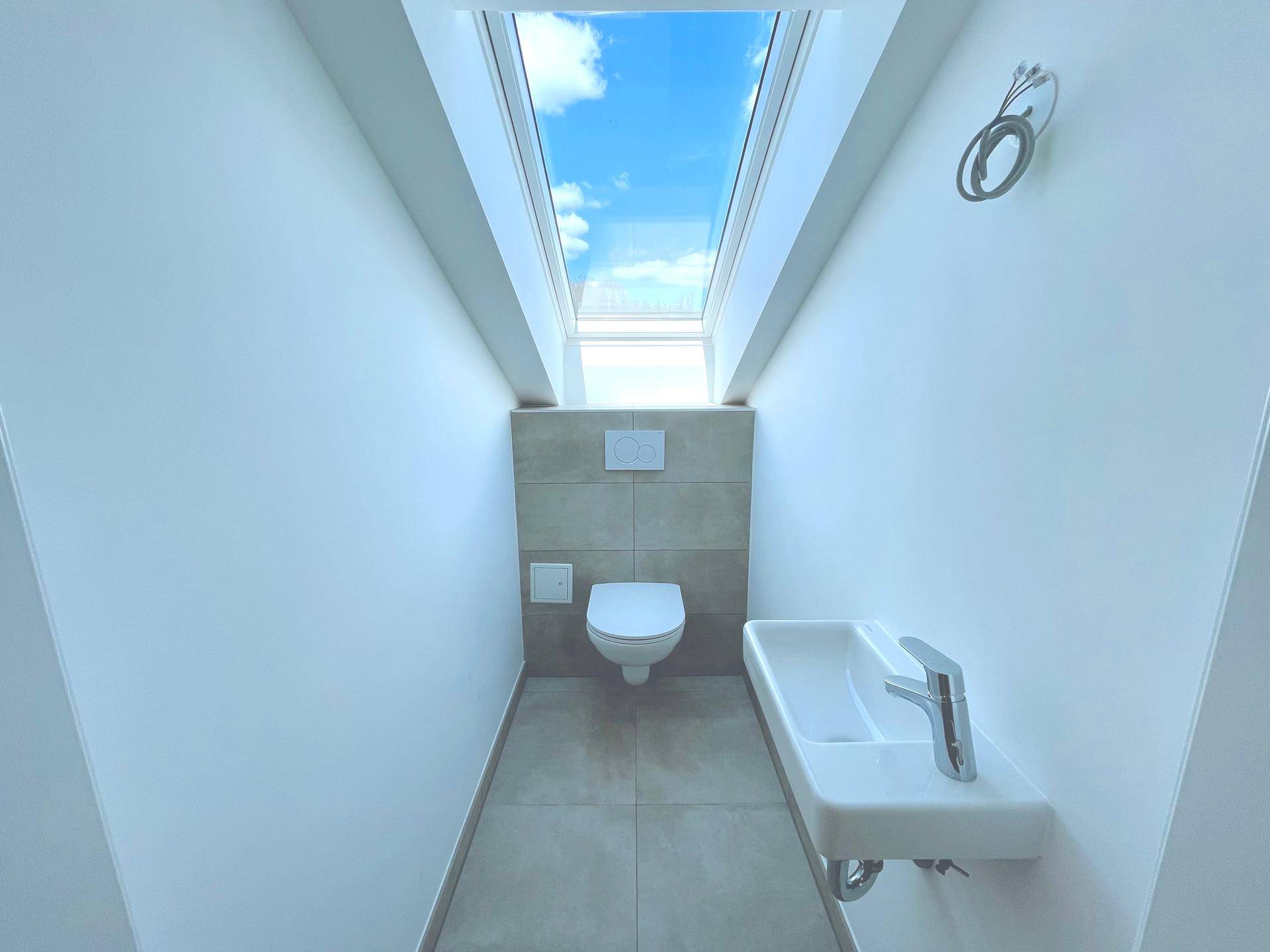 Separates Gäste-WC im Dachgeschoss mit Wand-WC, kleinem Waschbecken und Dachfenster, in modernem Design.