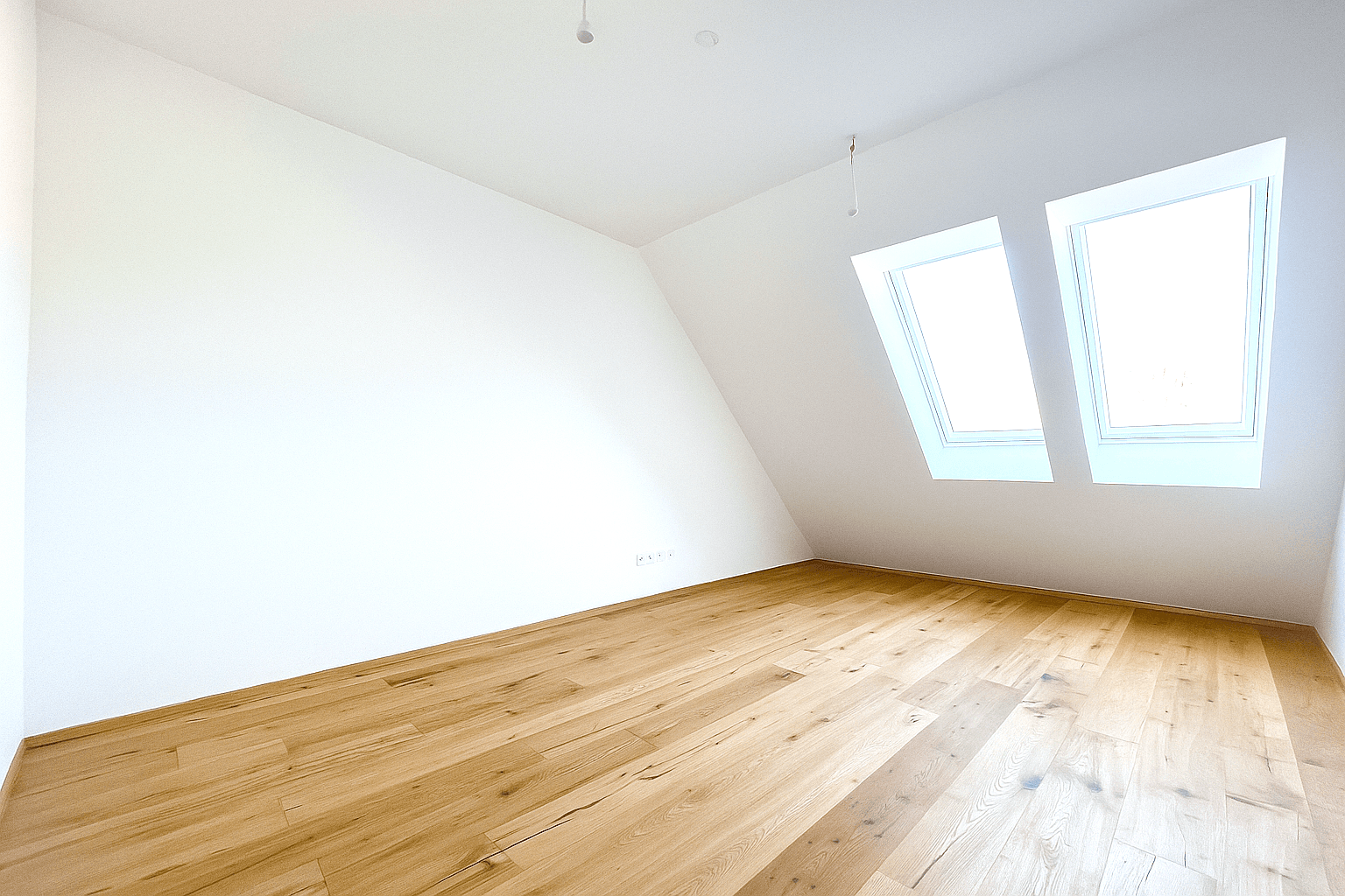 Geräumiges Schlafzimmer im Dachgeschoss mit Holzboden und zwei Dachfenstern, die den Raum erhellen.