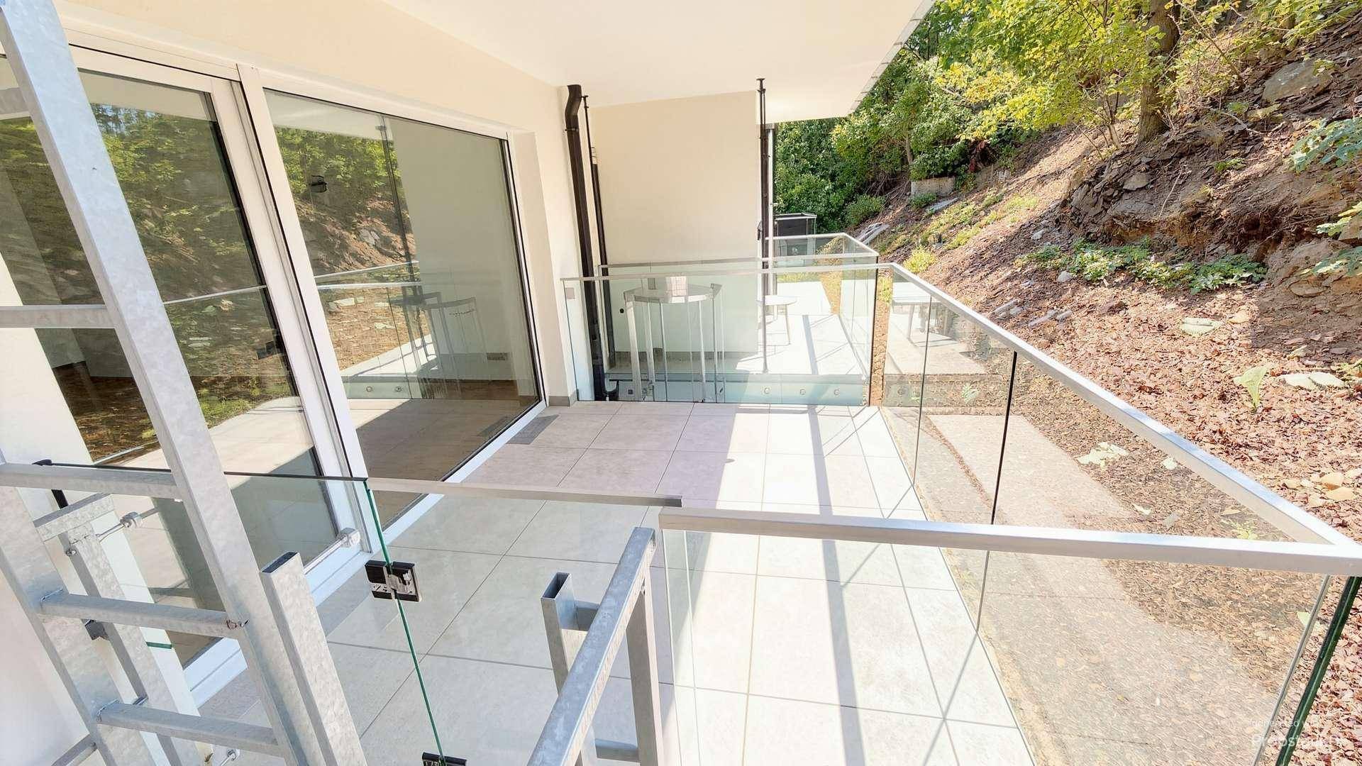 Geräumiger Balkon mit modernem Glasgeländer und Blick auf die bewaldete Hanglage.