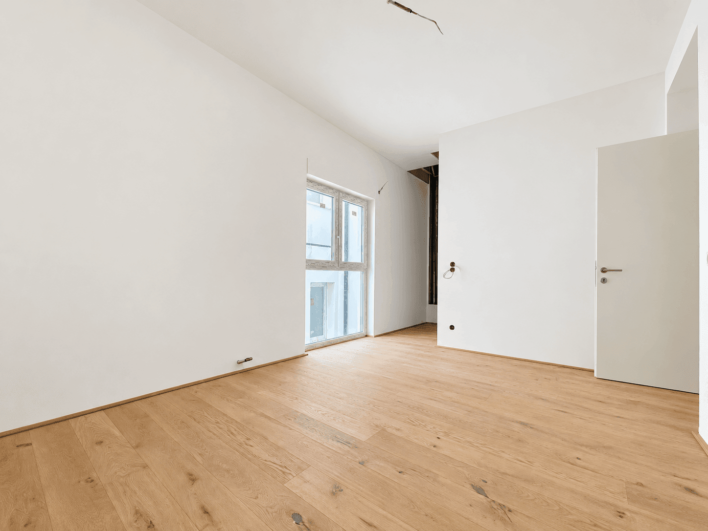 Lichtdurchflutetes Zimmer mit Holzboden und einer Tür, bereit für die individuelle Gestaltung.