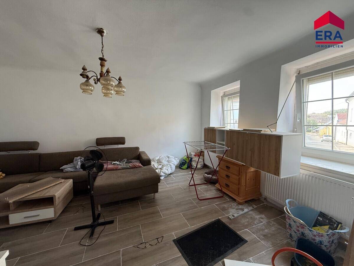Helles Wohnzimmer mit großem Ecksofa, modernen Fliesen und zwei Fenstern für viel Tageslicht.