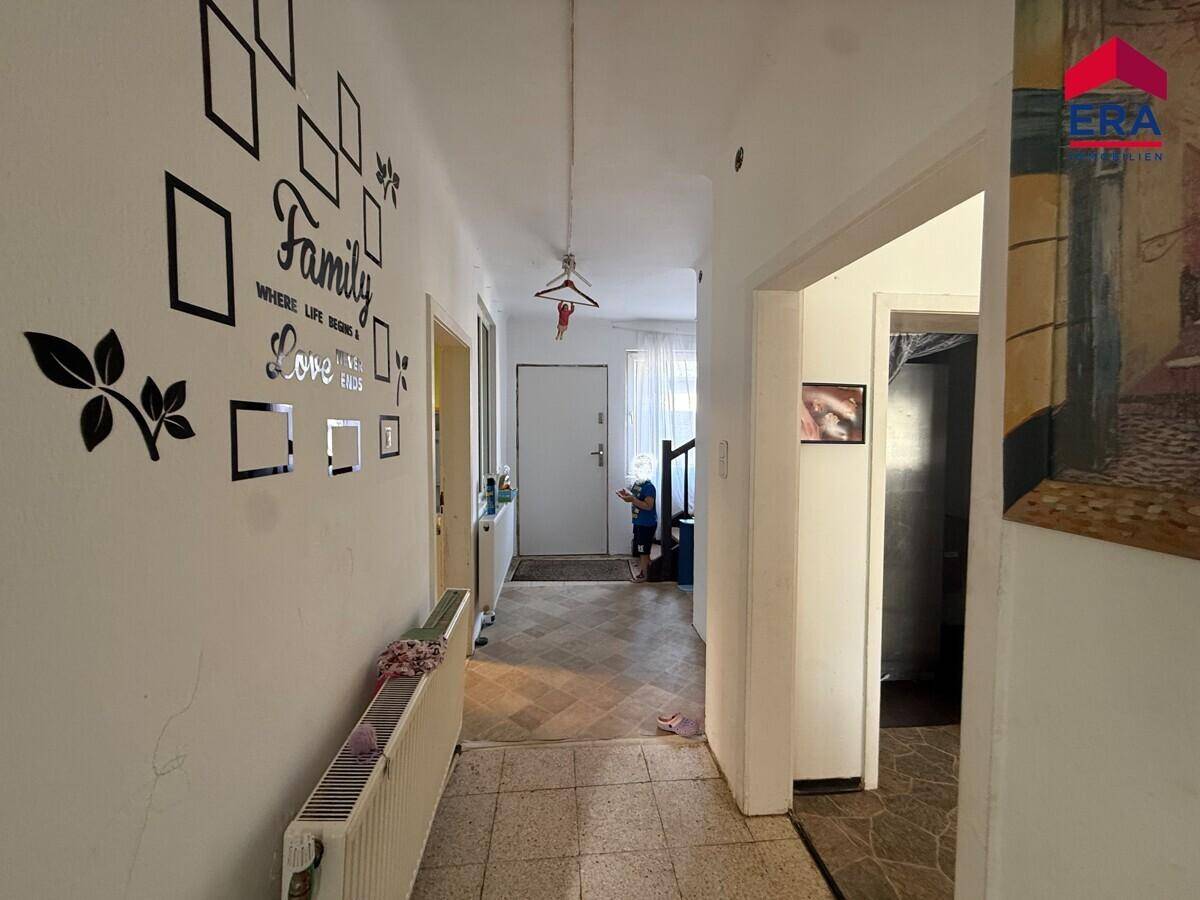 Langer Flur mit Fliesenboden und Wanddekoration, der zu weiteren Räumen führt.