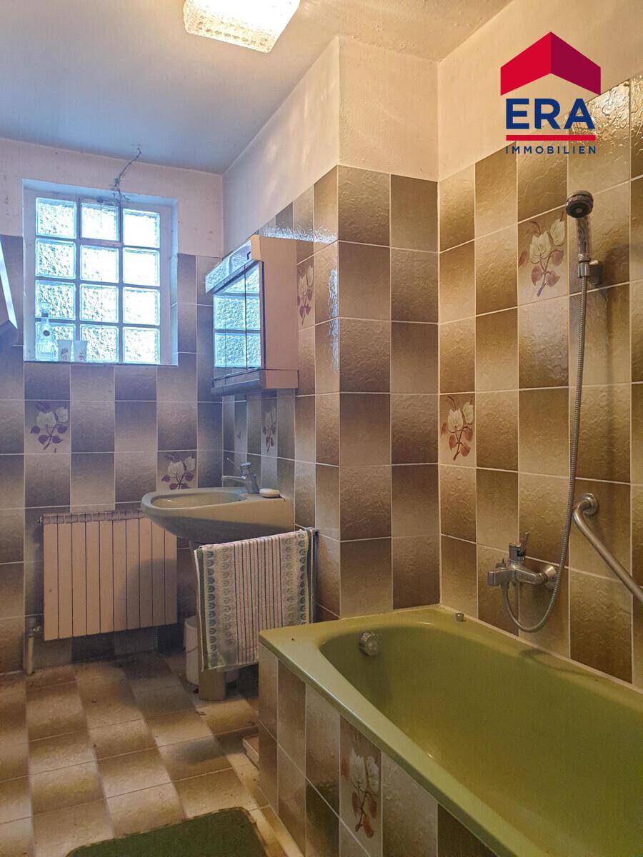 Badezimmer im 80er-Jahre-Stil mit grüner Badewanne, Waschbecken und Fliesen an Wänden und Boden.