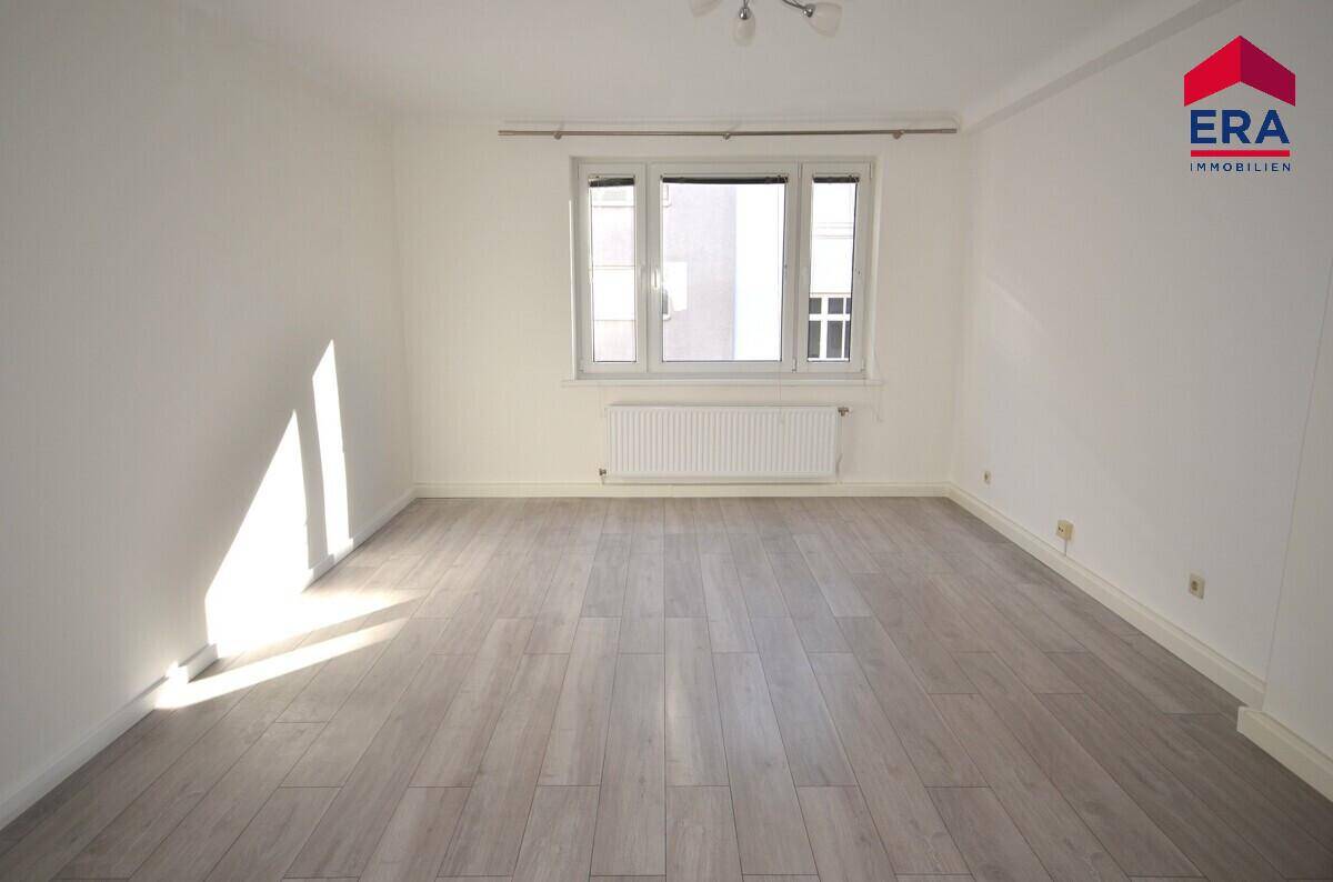 Lichtdurchflutetes Zimmer mit hellem Laminatboden und großen Fenstern, ideal für ein Wohn- oder Schlafzimmer.