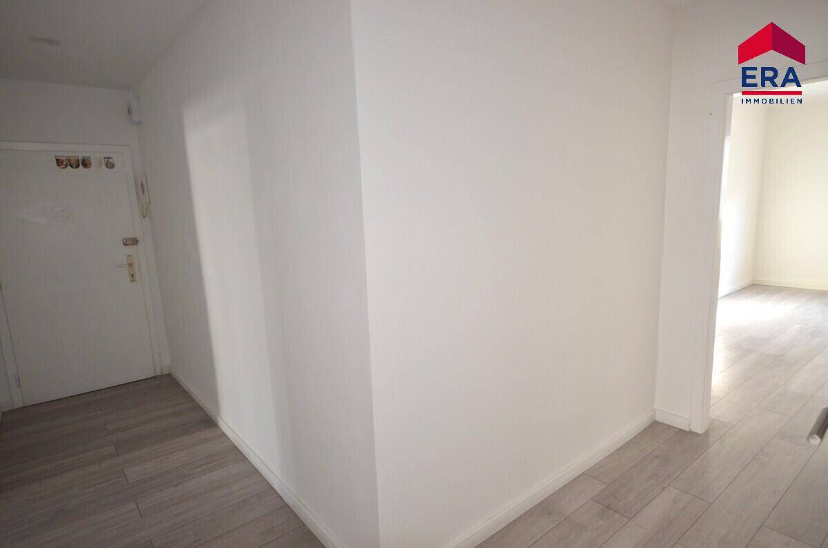 Heller Flur mit modernem Laminatboden und weißer Eingangstür, führt zu weiteren Räumen der Wohnung.