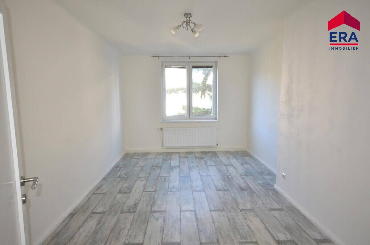Leeres Zimmer mit hellem Laminatboden und weiß gestrichenen Wänden, bietet vielseitige Nutzungsmöglichkeiten.