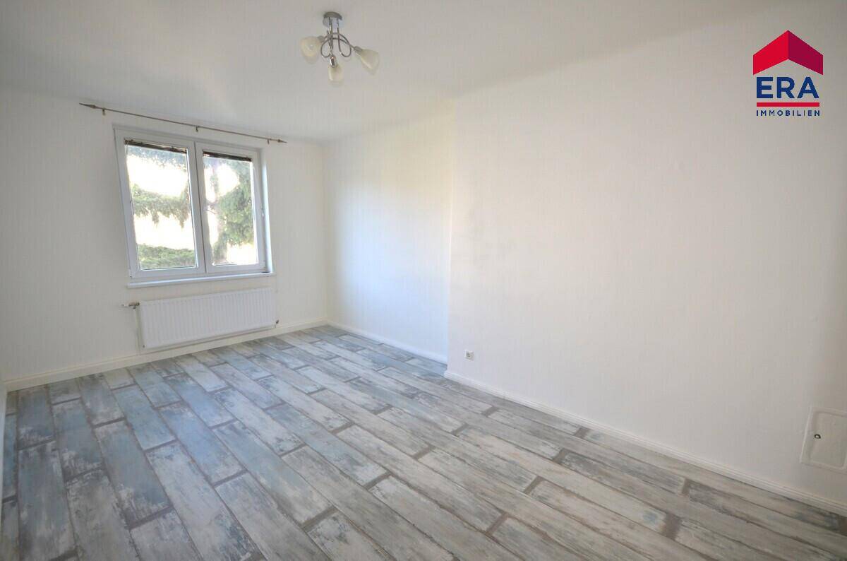 Geräumiges Zimmer mit hellem Laminatboden und Blick ins Grüne durch das Fenster, bietet viel Tageslicht.