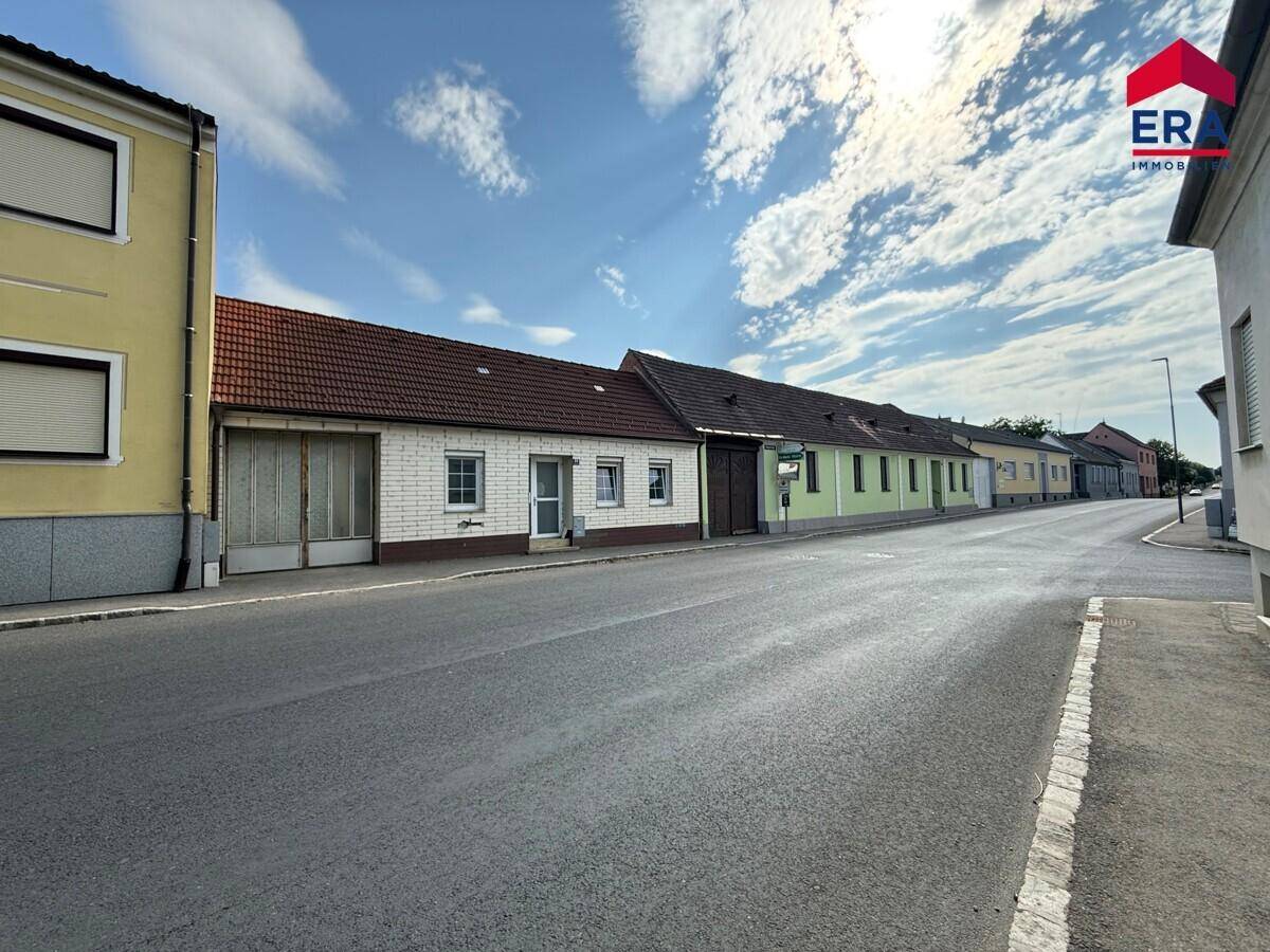 Blick auf die Straße mit dem Einfamilienhaus und angrenzenden Gebäuden unter blauem Himmel.