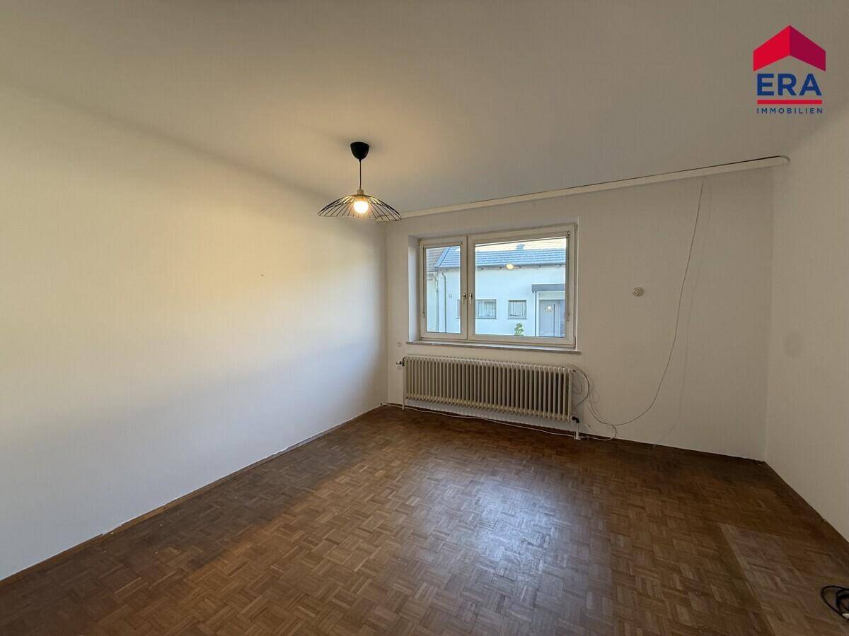 Helles Zimmer mit Parkettboden und großem Fenster, ideal als Wohn- oder Schlafzimmer.
