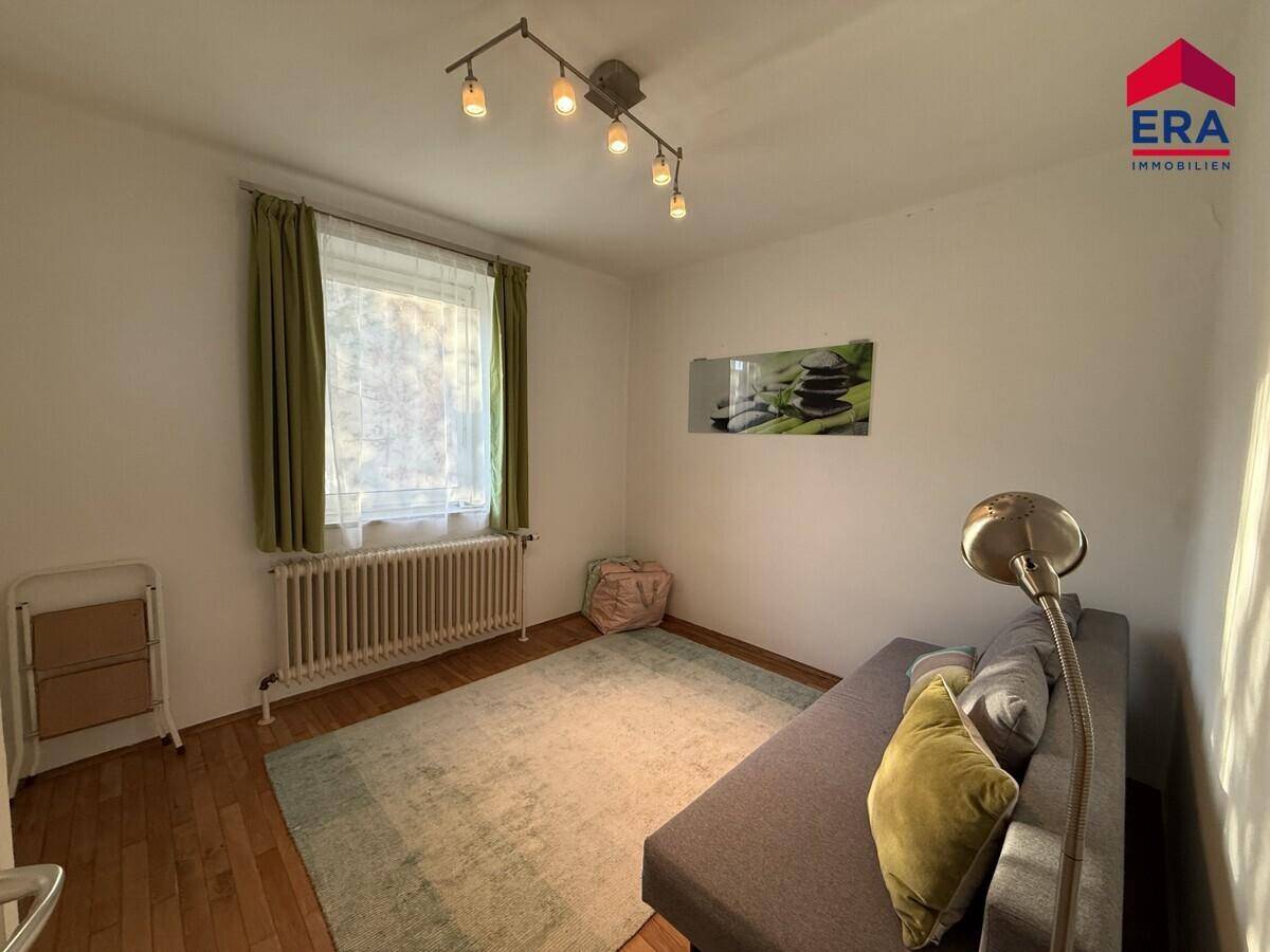 Gemütliches Wohnzimmer mit Sofa, Teppich und Fenster mit Vorhängen.