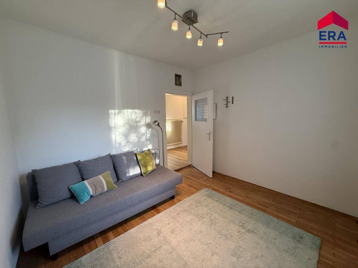 Gemütliches Wohnzimmer mit Sofa, Teppich und Fenster, das Tageslicht spendet.