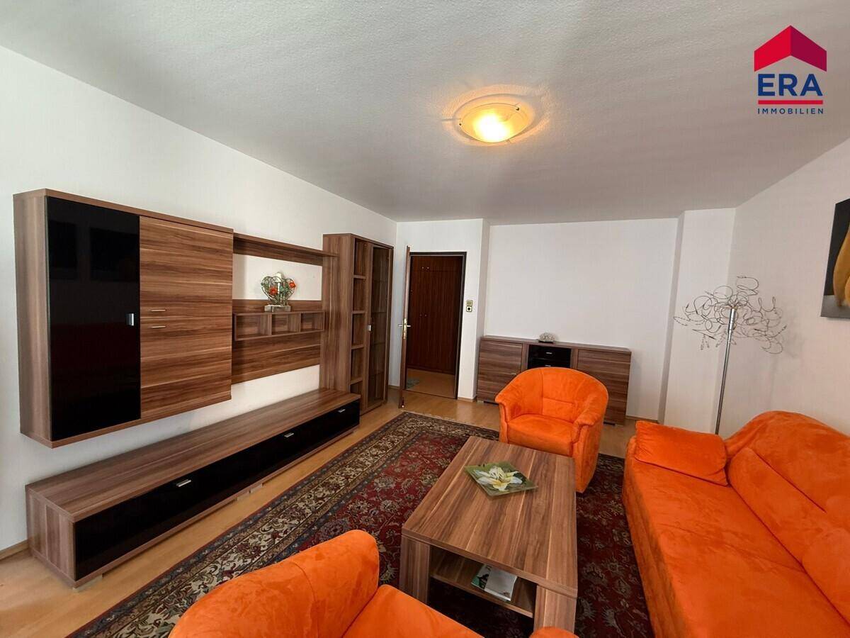 Wohnzimmer mit moderner Wohnwand aus Holz und dunklen Akzenten, sowie orangefarbenen Möbeln.