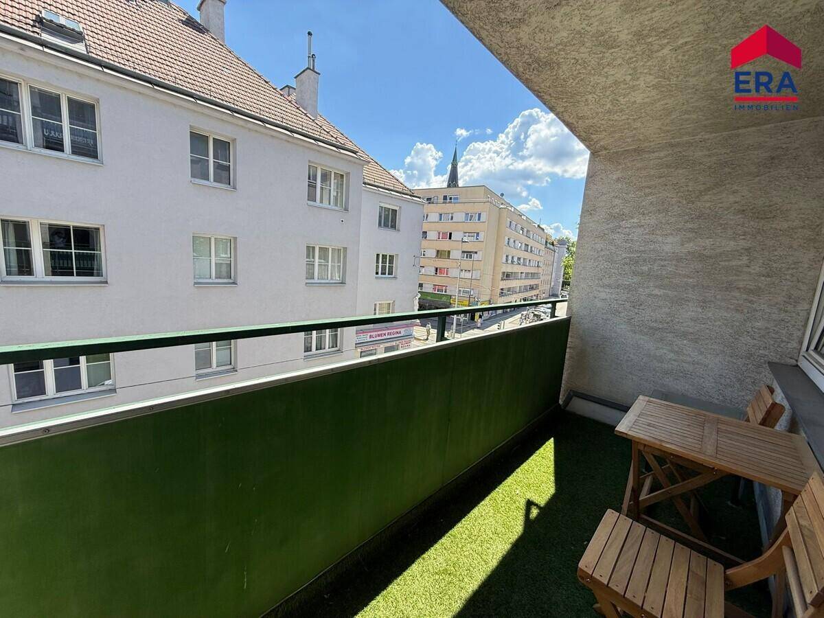 Balkon mit Blick auf die umliegenden Gebäude und die Stadt, ausgestattet mit Holztisch.