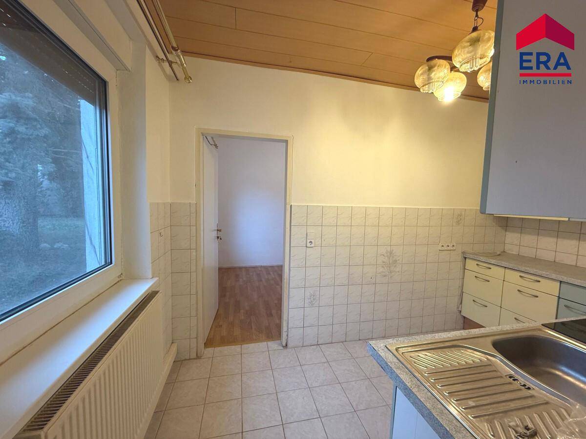 Küchenbereich mit Spüle, Fenster und gefliesten Wänden, bietet praktischen Arbeitsplatz.