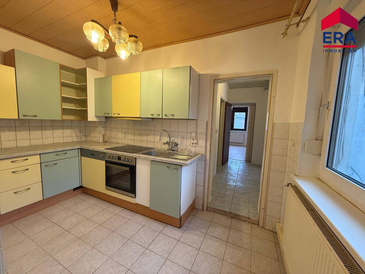 Küche mit bunten Schränken, Fliesenboden und Holzdecke, bereit zur Modernisierung.