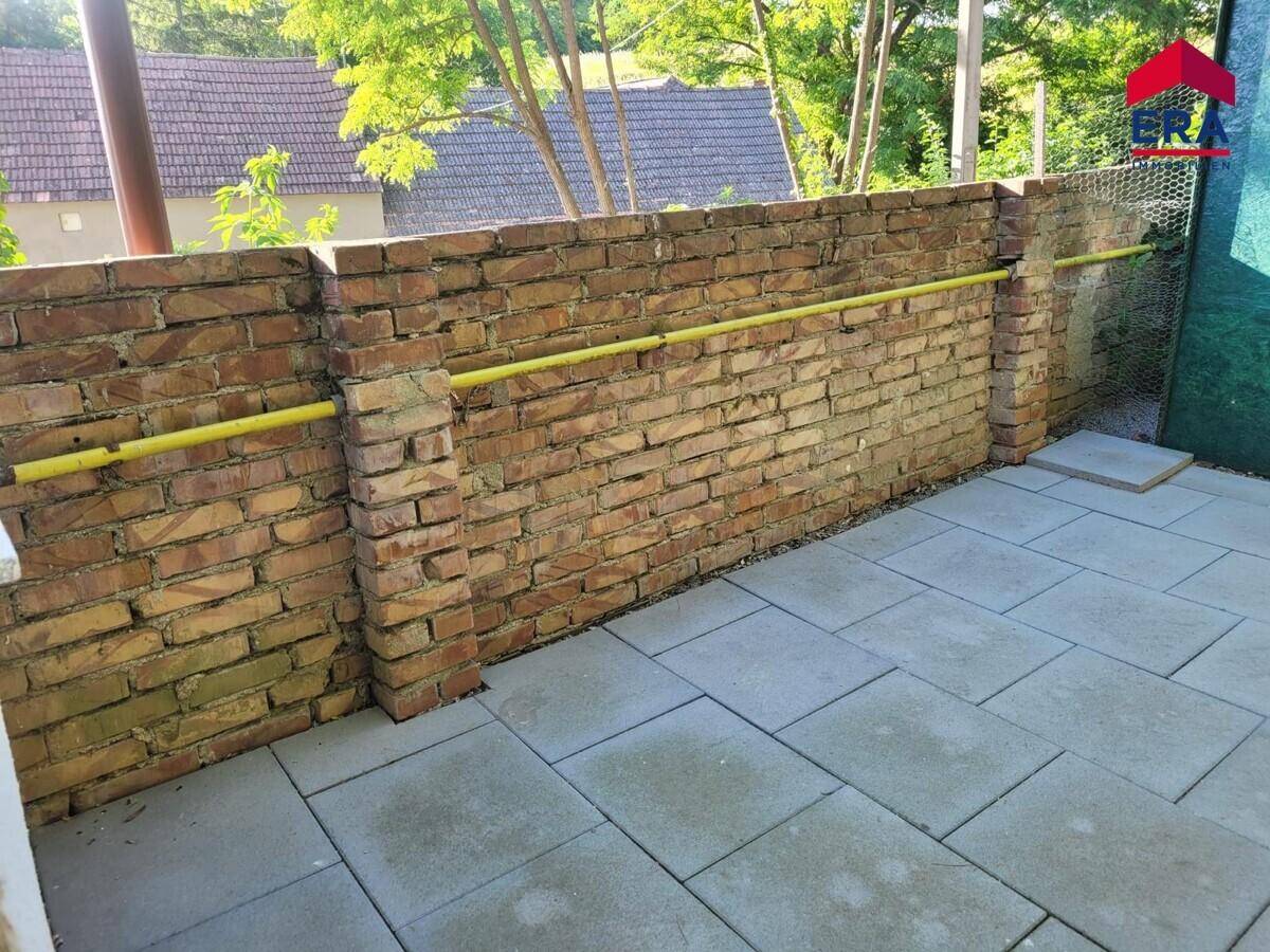 Gepflasterte Terrasse mit Ziegelmauer und gelbem Rohr, ideal für den Außenbereich.