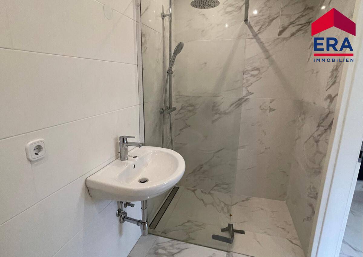 Helles Badezimmer mit moderner Dusche, Einzelwaschbecken und weißen Fliesen.