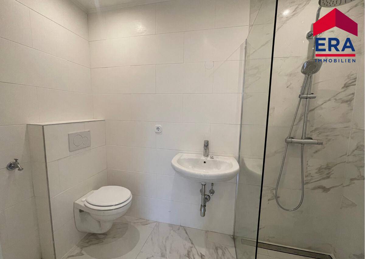 Modernes Badezimmer mit weißer Wand- und Bodenfliesen, wandhängendem WC und Dusche.