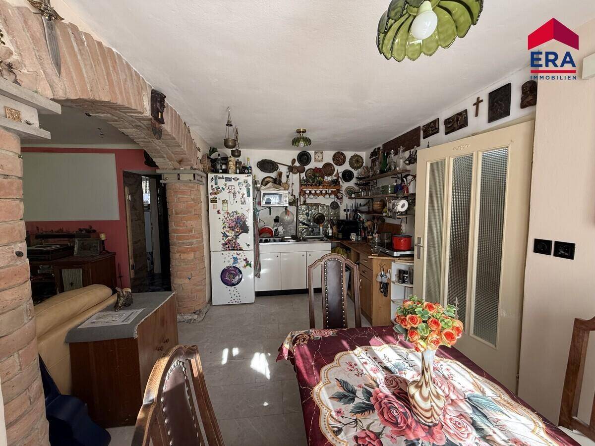 Rustikale Küche mit weißen Schränken, Kühlschrank und einem Esstisch, verbunden durch einen Ziegelbogen.