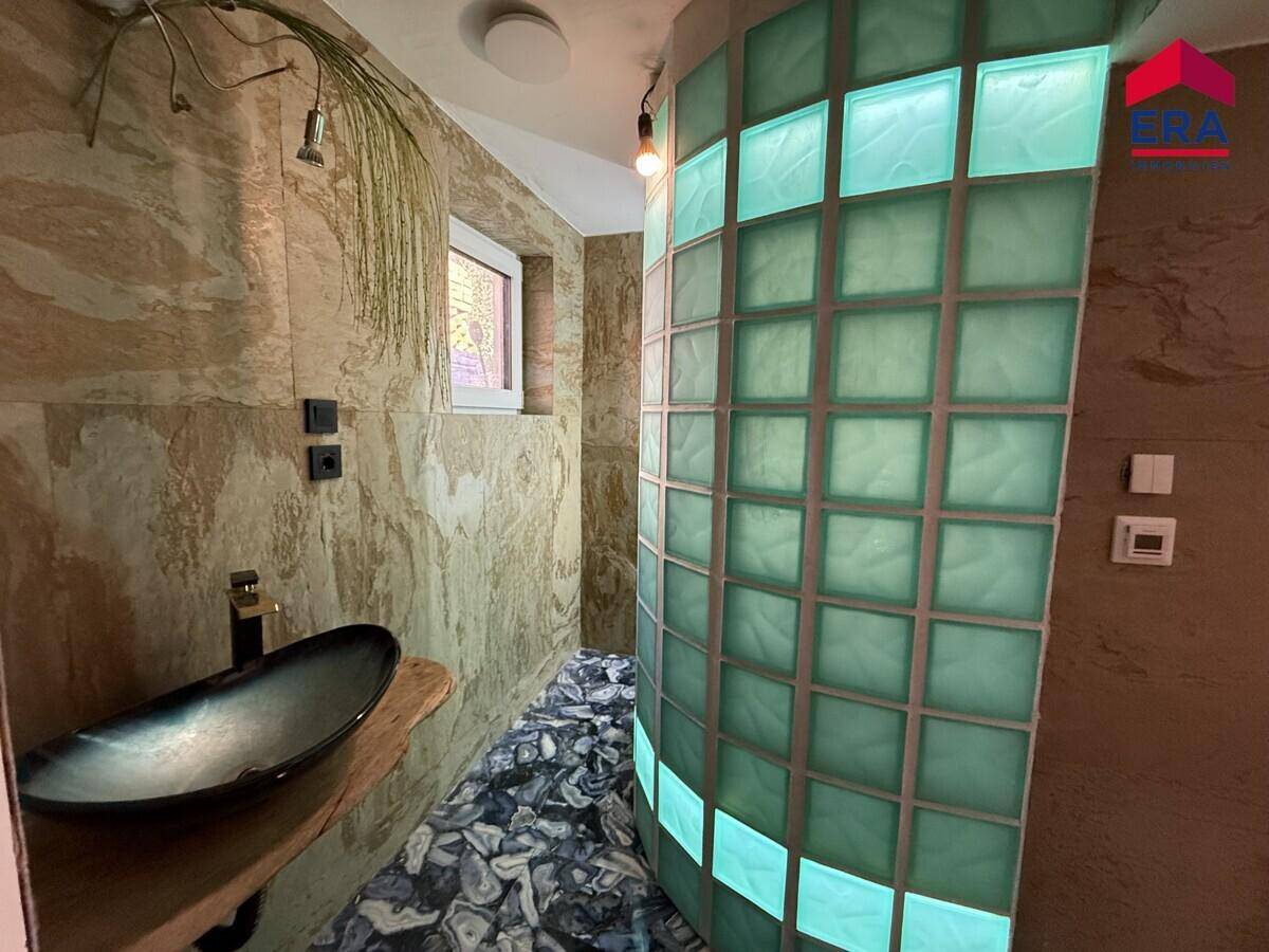 Modernes Badezimmer mit einzigartigem Waschbecken, strukturierten Wänden und einer Duschkabine aus Glasbausteinen.