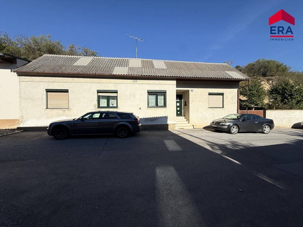 Vorderansicht eines Hauses mit schlichter Fassade, Satteldach und zwei geparkten Autos davor.
